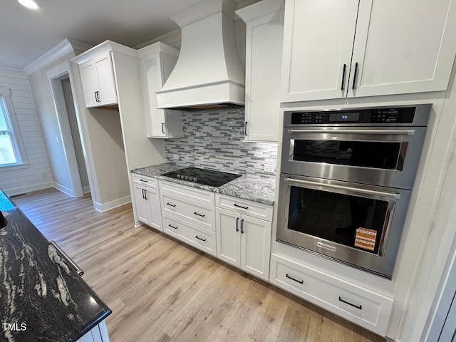 27 Batten Hill Ln, Selma, NC 27576 - kitchen with custom exhaust hood, stainless steel double oven, black electric stovetop, white cabinets, and light wood finished floors