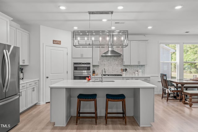kitchen with wall chimney range hood, appliances with stainless steel finishes, light countertops, decorative backsplash, and a kitchen bar