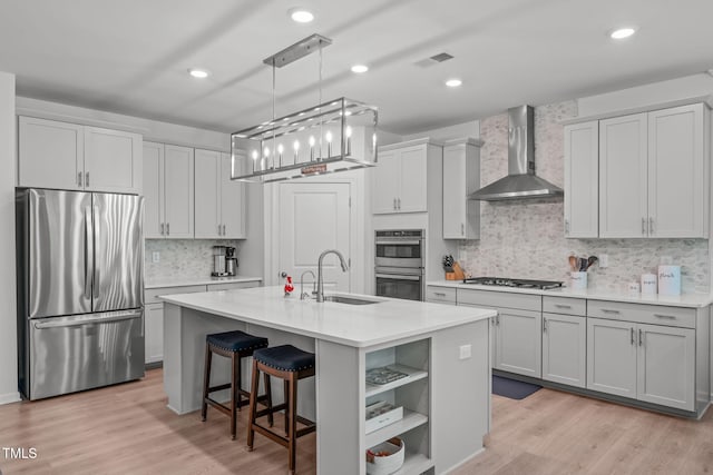 kitchen with wall chimney range hood, light countertops, a sink, backsplash, and stainless steel appliances