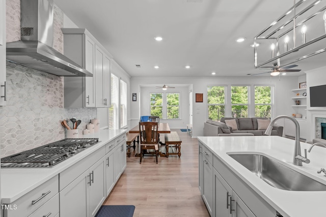 kitchen with a ceiling fan, stainless steel gas stovetop, a sink, and wall chimney exhaust hood