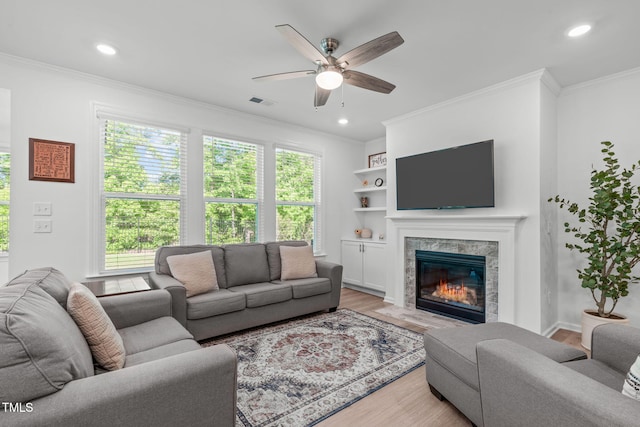 living room with crown molding, a ceiling fan, wood finished floors, and a high end fireplace