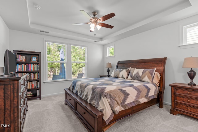 bedroom featuring a ceiling fan, light colored carpet, visible vents, baseboards, and a tray ceiling