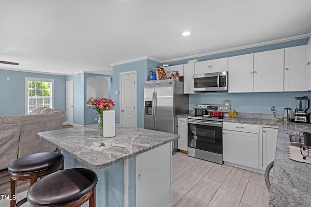 kitchen featuring crown molding, a breakfast bar, open floor plan, light stone counters, and stainless steel appliances