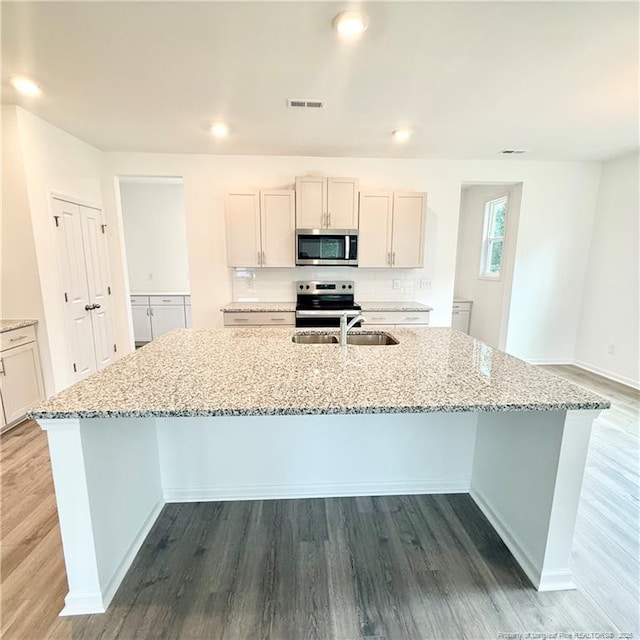 132 Cahill, Home, Raeford, NC 28376 - kitchen featuring stainless steel appliances, a sink, a center island with sink, light stone counters, and light wood-style floors