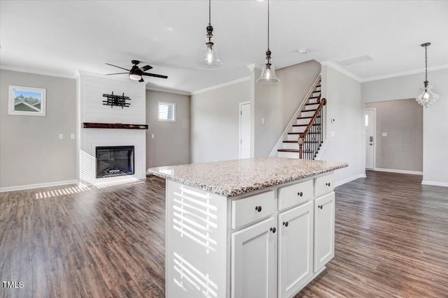 kitchen featuring ceiling fan, baseboards, open floor plan, ornamental molding, and a fireplace