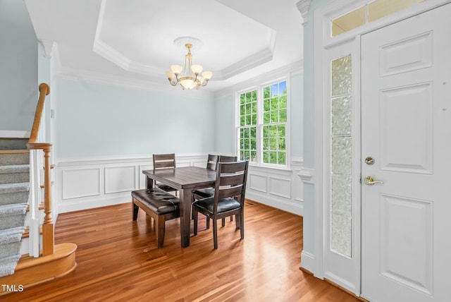 dining room featuring light wood-style flooring, stairway, a raised ceiling, ornamental molding, and a notable chandelier
