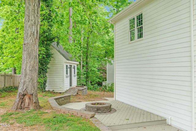view of property exterior featuring an outdoor structure, fence, and an outdoor fire pit