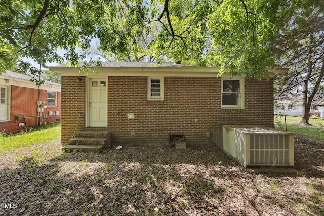 rear view of house with entry steps, fence, and brick siding