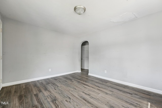 empty room featuring arched walkways, wood finished floors, and baseboards