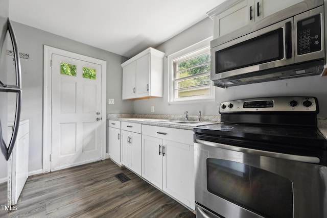kitchen with appliances with stainless steel finishes, a sink, white cabinetry, dark wood finished floors, and light countertops