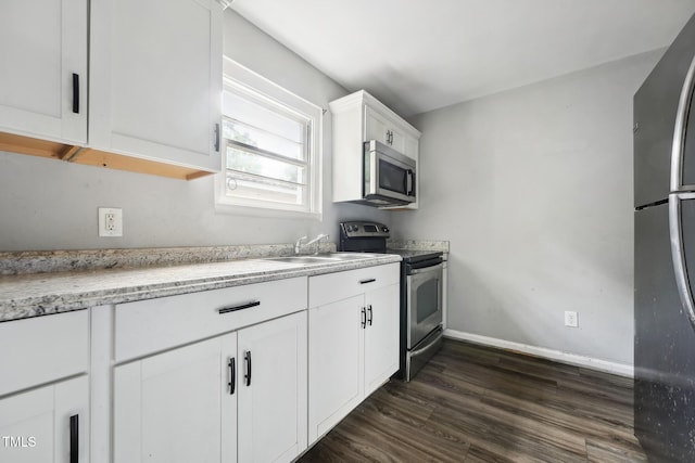 kitchen featuring appliances with stainless steel finishes, a sink, white cabinets, dark wood-type flooring, and baseboards