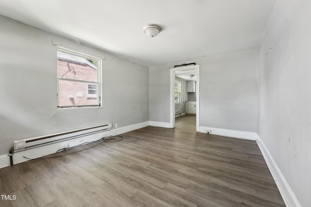 unfurnished bedroom featuring baseboard heating, a baseboard heating unit, multiple windows, and wood finished floors