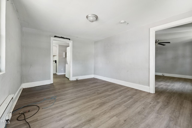 unfurnished room with baseboard heating, wood finished floors, and baseboards
