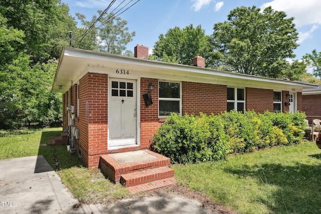 view of front of property with a chimney, brick siding, entry steps, and a front lawn