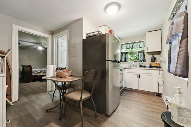 kitchen featuring freestanding refrigerator, white cabinets, light wood-type flooring, light countertops, and a sink