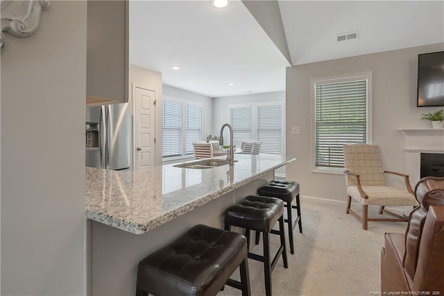 kitchen with a kitchen bar, a sink, stainless steel fridge, light colored carpet, and visible vents
