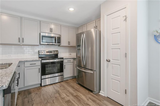 kitchen featuring light wood-style floors, tasteful backsplash, light stone countertops, and appliances with stainless steel finishes