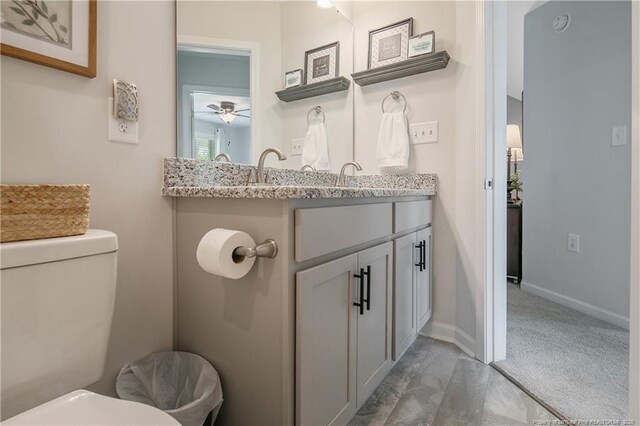 half bathroom featuring vanity, toilet, baseboards, and ceiling fan