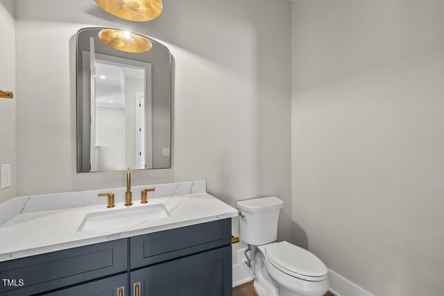 half bathroom with vanity, toilet, and baseboards