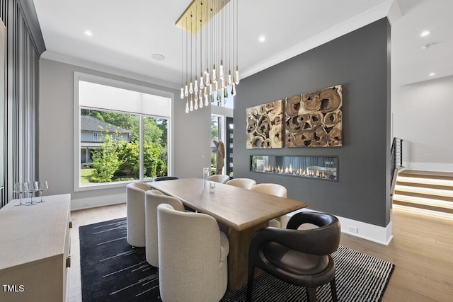 dining room with recessed lighting, a glass covered fireplace, baseboards, ornamental molding, and wood finished floors