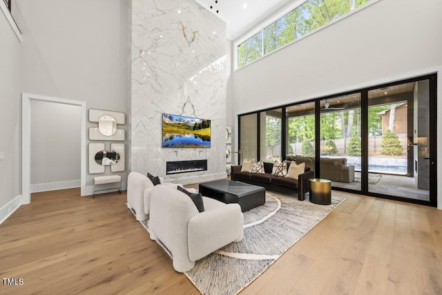 living room with a high ceiling, a premium fireplace, wood finished floors, and baseboards