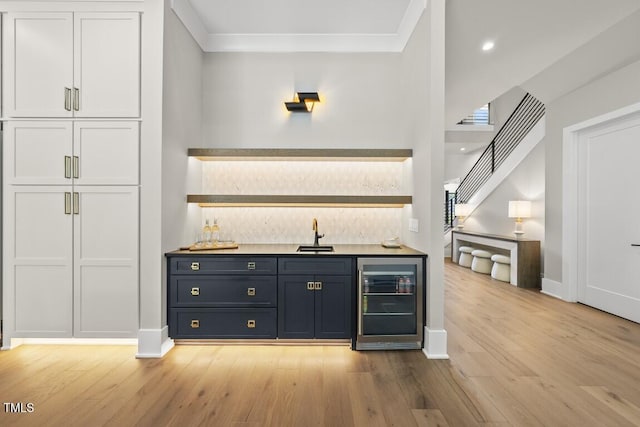 bar with wine cooler, light wood-style flooring, wet bar, and a sink