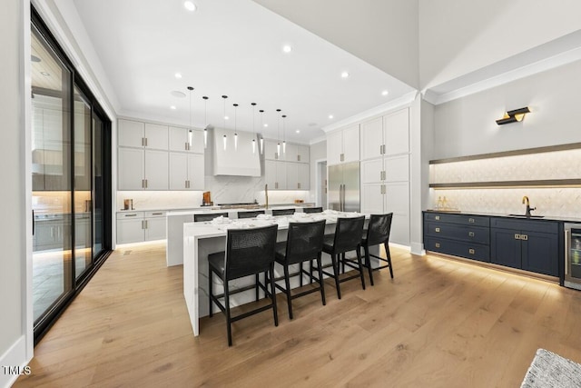 kitchen featuring a sink, decorative backsplash, built in refrigerator, a spacious island, and white cabinets