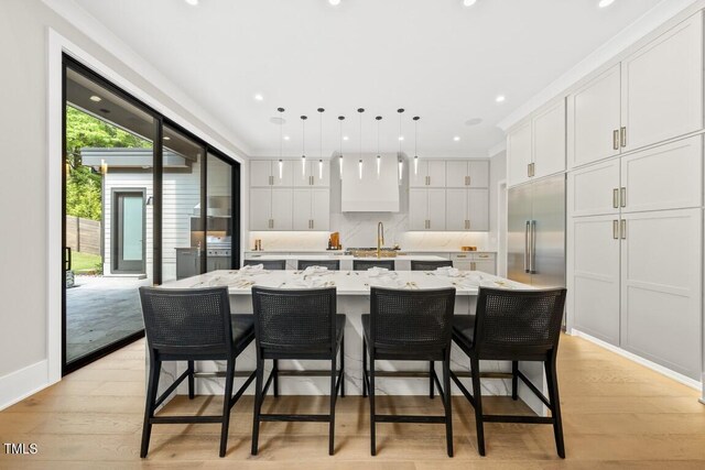 kitchen featuring built in fridge, white cabinets, a large island, light wood-type flooring, and pendant lighting