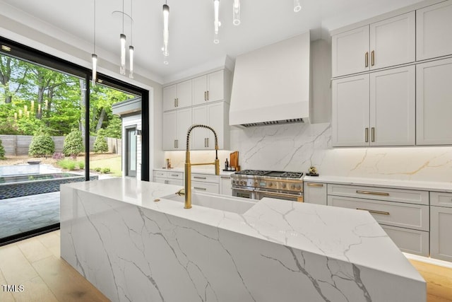 kitchen with range with two ovens, light wood-type flooring, custom exhaust hood, and a sink