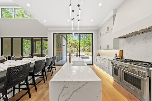 kitchen featuring custom exhaust hood, a kitchen island with sink, decorative backsplash, a sink, and range with two ovens