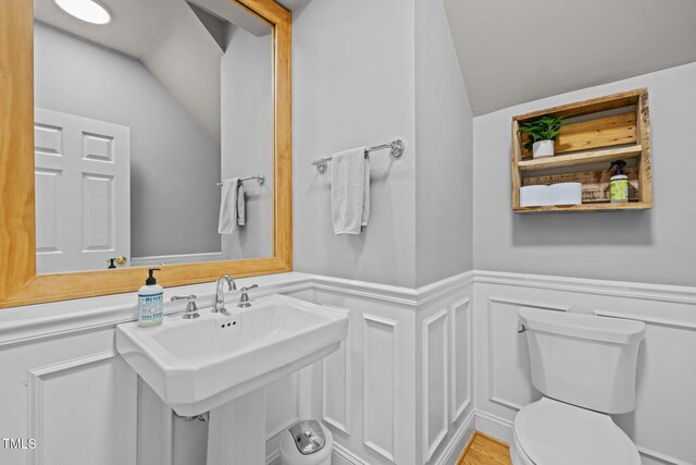 bathroom featuring toilet, wainscoting, lofted ceiling, and a decorative wall