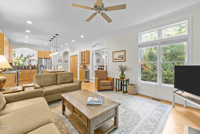 living room featuring visible vents, crown molding, arched walkways, ceiling fan with notable chandelier, and wine cooler