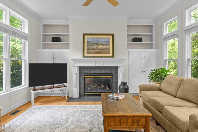 living area with ceiling fan, built in features, wood finished floors, visible vents, and ornamental molding
