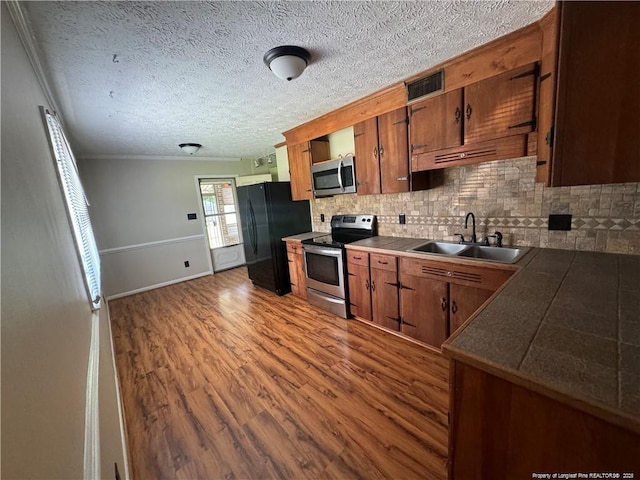 kitchen with dark wood-style floors, a sink, visible vents, appliances with stainless steel finishes, and ornamental molding