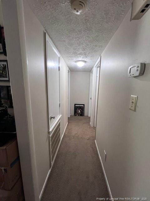 hall with carpet floors, a textured ceiling, and baseboards