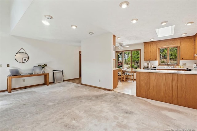 1619 Stonegate N, Sanford, NC 27332 - kitchen featuring brown cabinets, light countertops, light carpet, a skylight, and ceiling fan