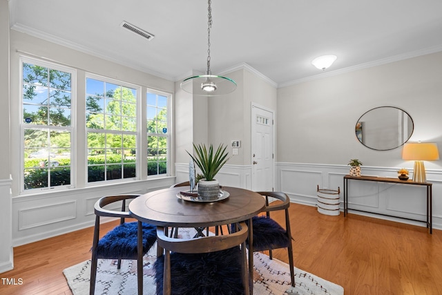dining room featuring ornamental molding, wood finished floors, wainscoting, and a decorative wall