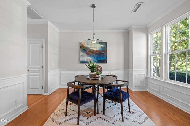 dining area with light wood finished floors, ornamental molding, wainscoting, and a decorative wall