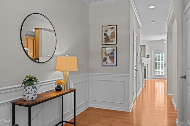hall with light wood-type flooring, crown molding, a wainscoted wall, recessed lighting, and a decorative wall