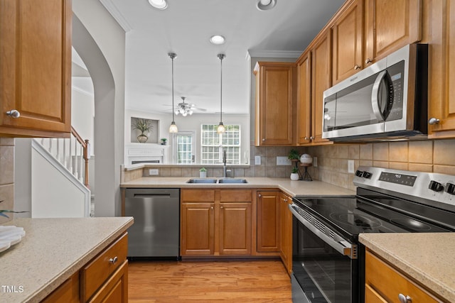 kitchen with stainless steel appliances, a sink, light wood-type flooring, brown cabinetry, and backsplash