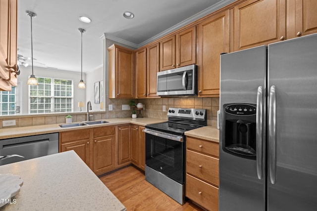 kitchen with appliances with stainless steel finishes, a sink, light countertops, ornamental molding, and light wood-type flooring