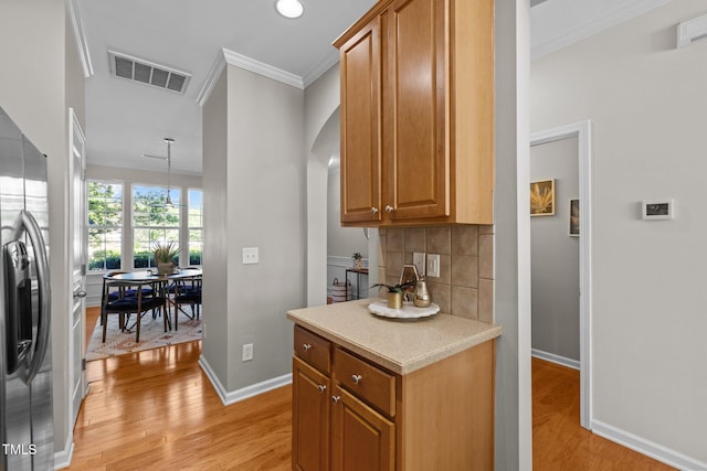 kitchen featuring light wood finished floors, baseboards, light countertops, stainless steel fridge, and tasteful backsplash