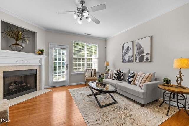 living room with ornamental molding, wood finished floors, ceiling fan, a fireplace with flush hearth, and baseboards