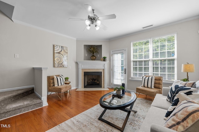living area featuring ceiling fan, wood finished floors, a fireplace, crown molding, and baseboards