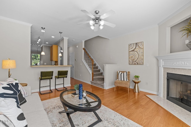 living area with crown molding, a ceiling fan, wood finished floors, a high end fireplace, and stairs