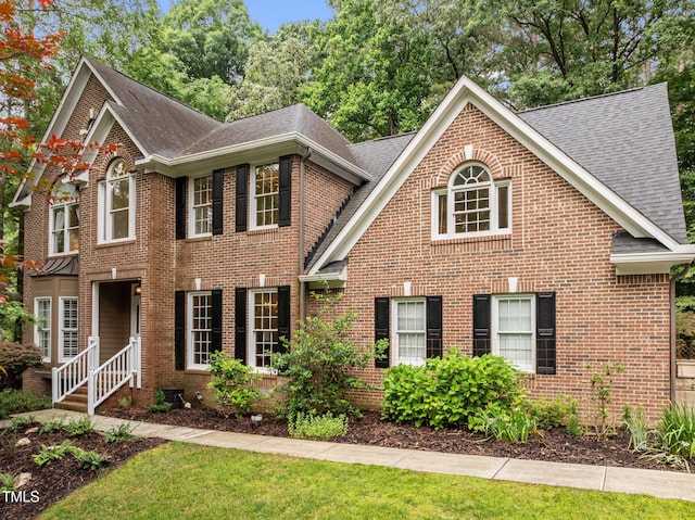 colonial-style house with roof with shingles, brick siding, and a front lawn