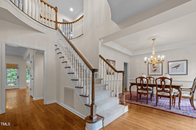 stairs with ornamental molding, wood finished floors, a chandelier, and baseboards