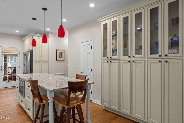 kitchen featuring high end refrigerator, light stone countertops, light wood-style floors, pendant lighting, and glass insert cabinets