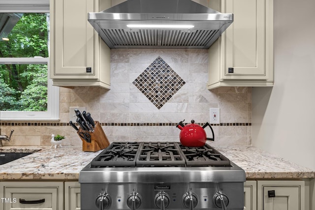 kitchen with extractor fan, decorative backsplash, light stone counters, stove, and cream cabinets