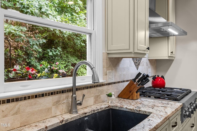 kitchen featuring range hood, backsplash, light stone countertops, a sink, and white cabinetry